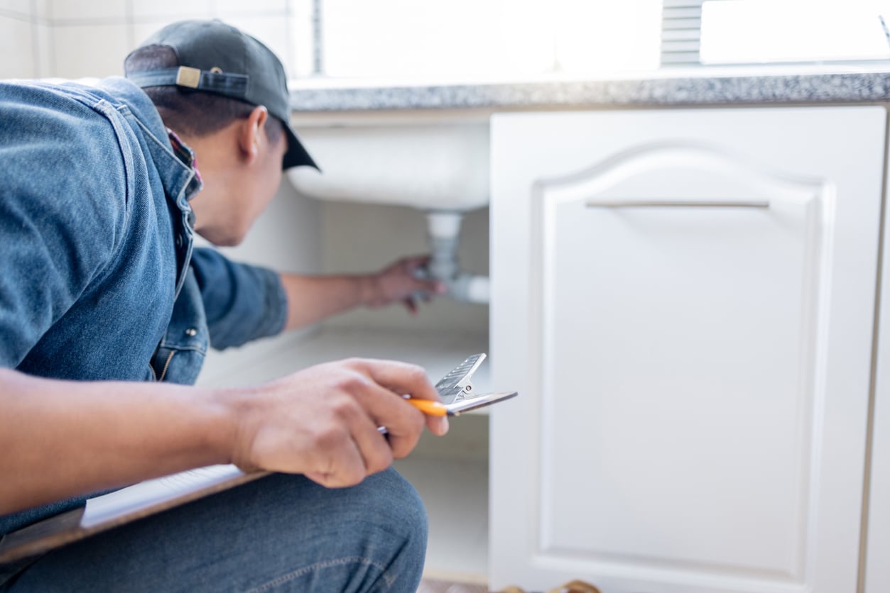 Plumber inspecting residential plumbing pipes and water connections inside a Metro Atlanta home